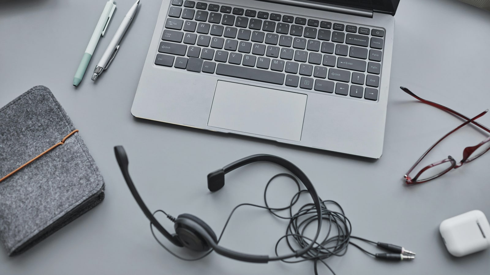 A calm support desk workspace with a laptop, notebook, and headphones.